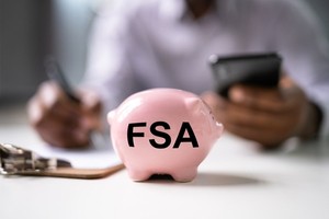 A man noting down FSA details from his mobile to paper and FSA written piggie bank is placed near the clipboard