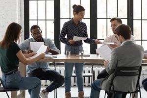 biracial female mentor trainer giving millennial trainees students paper documents by subject matter to educate