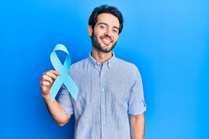 hispanic man holding blue ribbon looking positive and happy standing and smiling
