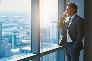 mature business ceo talking on phone alongside large high windows