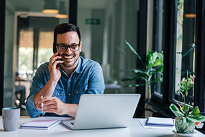 A man is on the phone smiling at his desk.