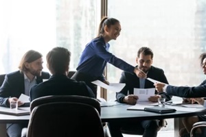 happy businesswoman manager gives employee benefits risk management handout in boardroom at meeting