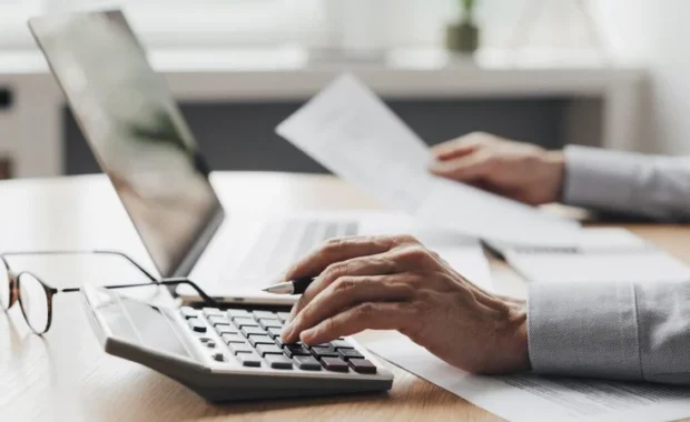 Person-with-Calculator-and-Laptop-and-Paperwork-1200-627
