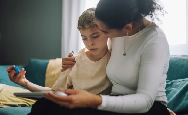 Mother-with-arm-around-son-sitting-on-sofa-at-home_tmb