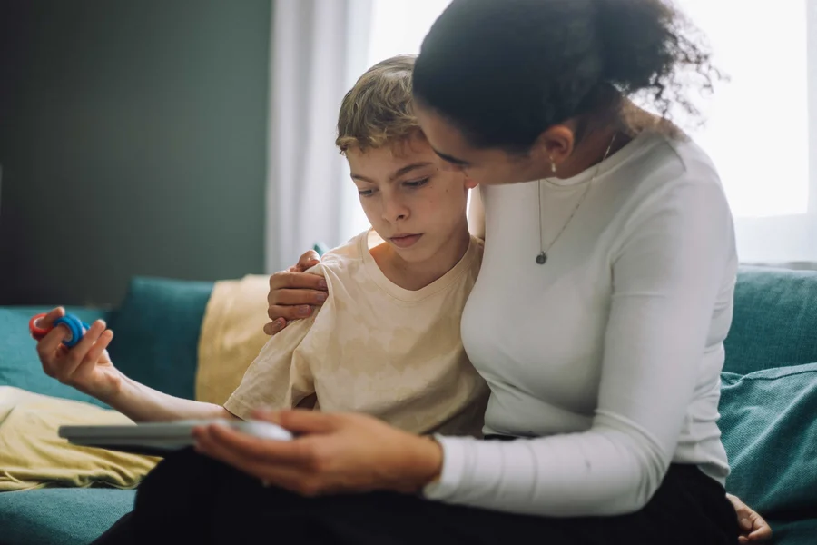 Mother-with-arm-around-son-sitting-on-sofa-at-home_tmb